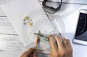 Sharpens the pencil with a knife. Clock, notepad and mobile phone desk.