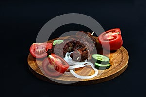 Shashlick and cut vegetables on wooden cutting board on black background