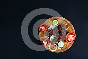 Shashlick and cut vegetables on wooden cutting board on black background flat lay