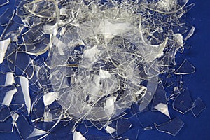 Shattered into 1000 shards concept: View on isolated pile broken glass fragments, blue background