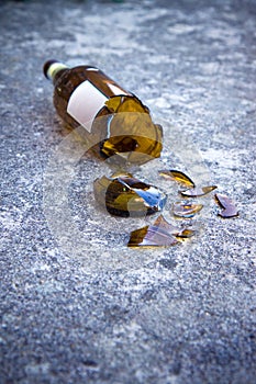 Shattered brown beer bottle resting on the ground: alcoholism co