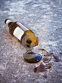 Shattered brown beer bottle resting on the ground: alcoholism concept