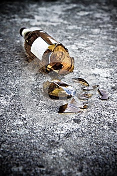 Shattered brown beer bottle resting on the ground: alcoholism concept