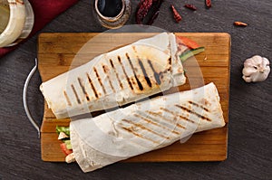 Shaurma chicken roll in a pita with fresh vegetables and cream sauce composition on wooden background