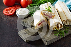 Shaurma lavash with fried chicken meat, fresh vegetables and creamy sauce on a background of brown stone.