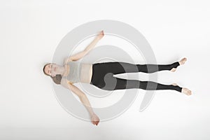 Shavasana. Corpse Pose. Yoga asanas. Young slender woman in sportswear lies on the white floor . Top view