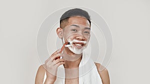 Shave everyday. Portrait of shirtless young asian man with towel around his neck shaving his face, looking at camera