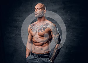 Shaved head, muscular male with tattoos on his torso over grey v