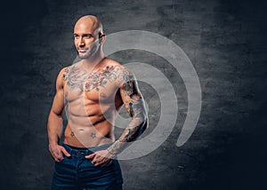 Shaved head, muscular male with tattoos on his torso over grey v