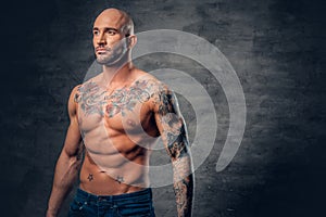 Shaved head, muscular male with tattoos on his torso over grey v