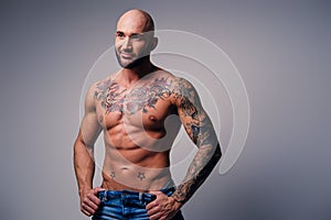 Shaved head, muscular male with tattoos on his torso over grey v