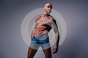 Shaved head, muscular male with tattoos on his torso over grey v