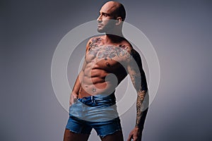 Shaved head, muscular male with tattoos on his torso over grey v