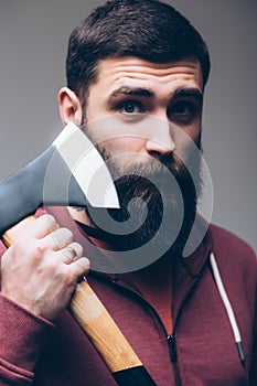 Shaving with axe. Confident young bearded man carrying a big axe