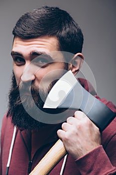 Shaving with axe. Portrait of Confident young bearded man carrying a big axe on shoulder and looking at camera