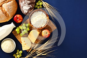 Shavuot food on blue background. Flat lay Jewish delicious dishes, cottage cheese, bottle of milk, cereal bread, grape, apples,