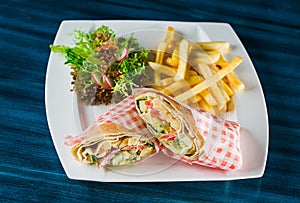 Shawarma chicken roll in a pita with fresh vegetables and cream sauce on wooden background. Selective focus