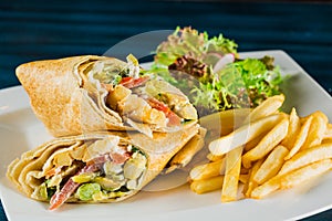 Shawarma chicken roll in a pita with fresh vegetables and cream sauce on wooden background. Selective focus
