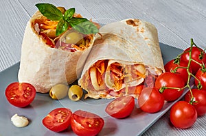 Shawarma sandwich or lavash with fresh vegetables and sauce on the gray plate decotated with cherry tomatoes, basil leaves