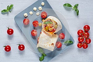 Shawarma sandwich or lavash snack with fresh vegetables on the gray plate decotated with cherry tomatoes, basil leaves, sauce
