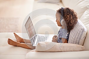 Shea already so studious. a little girl using headphones and a laptop while sitting at home.