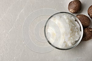 Shea butter in bowl and nuts on table, top view.