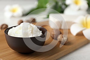 Shea butter in bowl and nuts on wooden board, closeup.