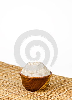 Shea butter in the wooden bowl stands on the straw mat, clean white background.