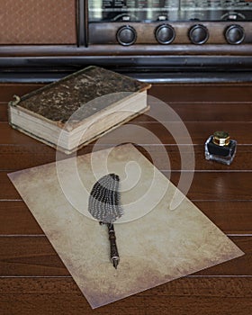 A sheet of antiqued paper with a fountain pen with a feather on it, on a wooden table with a bottle of ink next to it