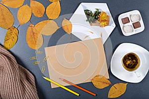 Sheet of brown craft paper, white envelope with note and flower, yellow and orange leaves, color pencils, cup of herbal tea and c