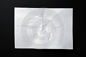 A sheet of crumpled white paper on a black background.Crumpled white paper background. Wrinkled sheet texture, top view.