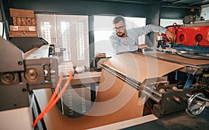 Sheet cutting machine. Operating device. Print house worker in white clothes is indoors