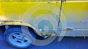 Sheet metal corrosion over wheel of old yellow car. Rusty messy surface. Damaged grunge dirty texture from road salt. Rust