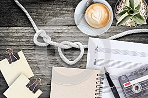 Sheet music, cactus, fountain pen, tape cassette and coffee latte on vintage wooden table