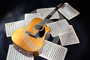 sheet music scores and classical acoustic six-string yellow guitar with black pickguard on isolated black background