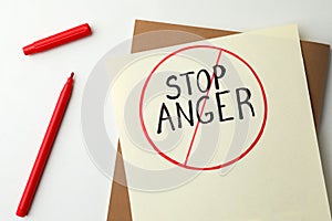 Sheet of paper with crossed over inscription Stop Anger and red felt tip pen on white table, flat lay