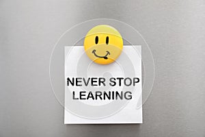 Sheet of paper with phrase NEVER STOP LEARNING and magnet on refrigerator door