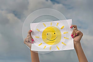 Sheet of paper with sun image against overcast sky