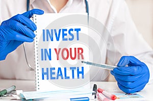 A sheet of paper with text INVEST IN YOUR HEALTH, stethoscope and medical documents on the table. Medical concept