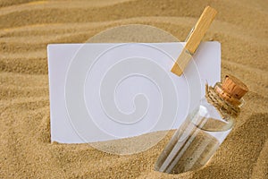 Sheet of white paper with copy space clothespin Paper Message in a glass bottle with a cork on the sand. Summer vacation