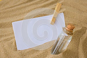 Sheet of white paper with copy space clothespin Paper Message in a glass bottle with a cork on the sand. Summer vacation