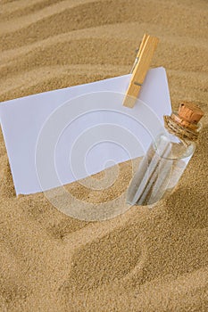 Sheet of white paper with copy space clothespin Paper Message in a glass bottle with a cork on the sand. Summer vacation
