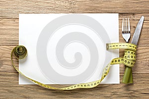 Sheet of white paper on the wooden desk with knife and fork wrap