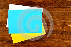 Sheet of white, yellow and blue office paper lie on a wooden background, sticker on wooden table, copy space