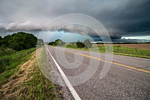 A shelf cloud and severe storm filled with rain and hail approach a highway.