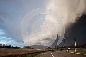 A shelf cloud and severe thunderstorm approaches rapidly with a road and streetlights in the foreground.