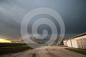 A shelf cloud and storm approach old farm buildings in the Midwest.