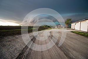 A shelf cloud and storm approach old farm buildings at sunset.