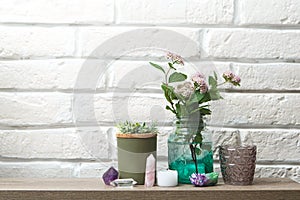 A shelf for decorative ornaments. Home-made beautiful things. Crystals, candlesticks, flowers in a jar against a white brick wall