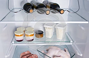On the shelf of the refrigerator are food, three bottles of wine, dairy bio-products, meat, chicken and steaks